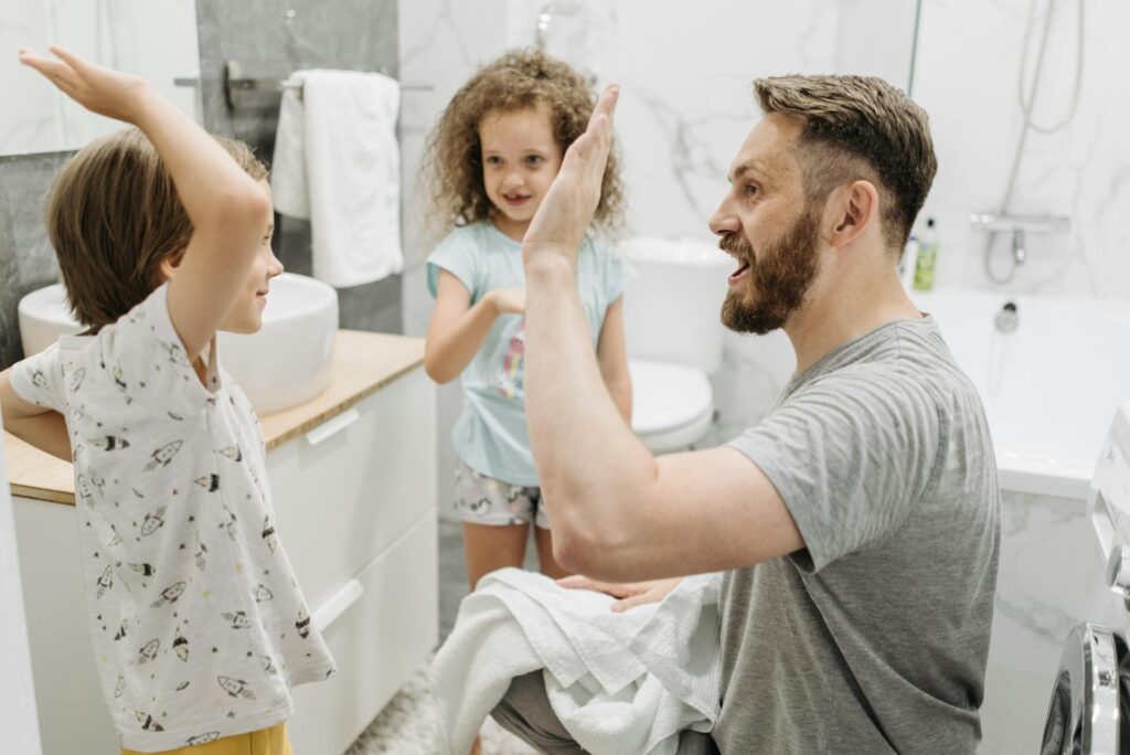 Vater und zwei Kinder genießen eine fröhliche Zeit im modernen Badezimmer mit sicheren Waschtischarmaturen und kinderfreundlicher Ausstattung.