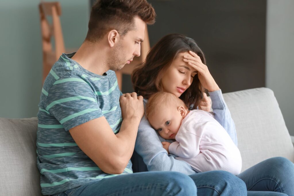 Trauernde Eltern mit Baby auf Sofa.