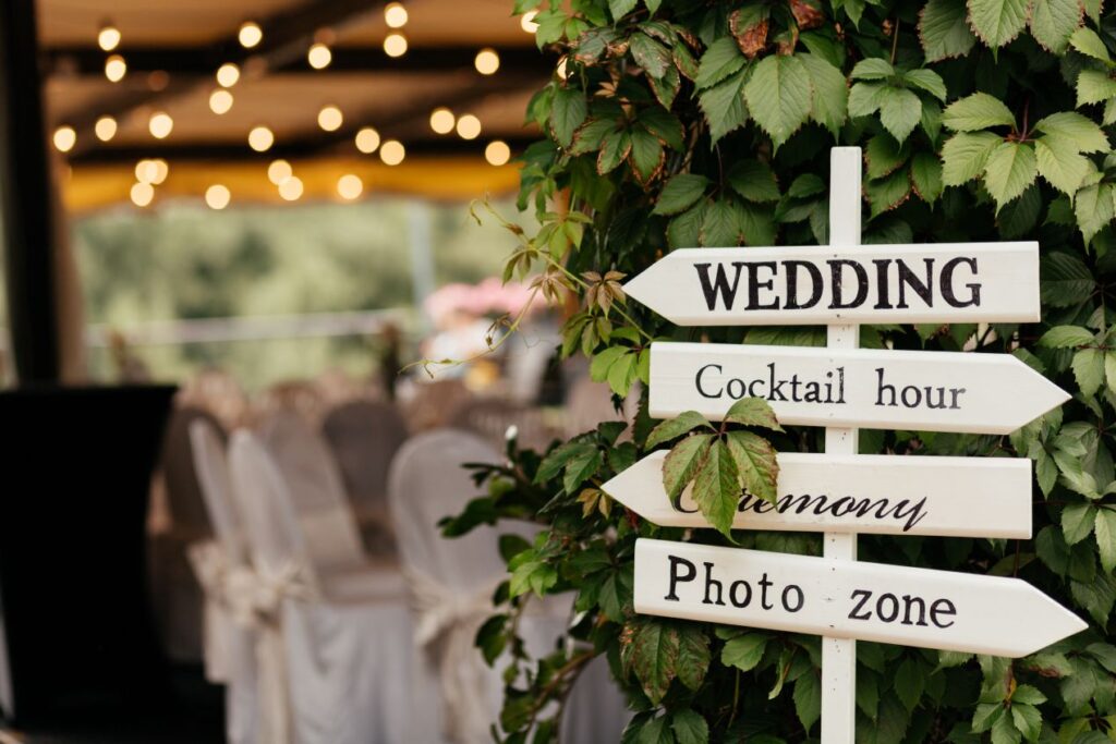 Hochzeit auf dem Bauernhof: stilvoller Wegweiser mit Hinweisen zu Ceremony, Cocktail Hour und Photo Zone vor gruener Naturkulisse