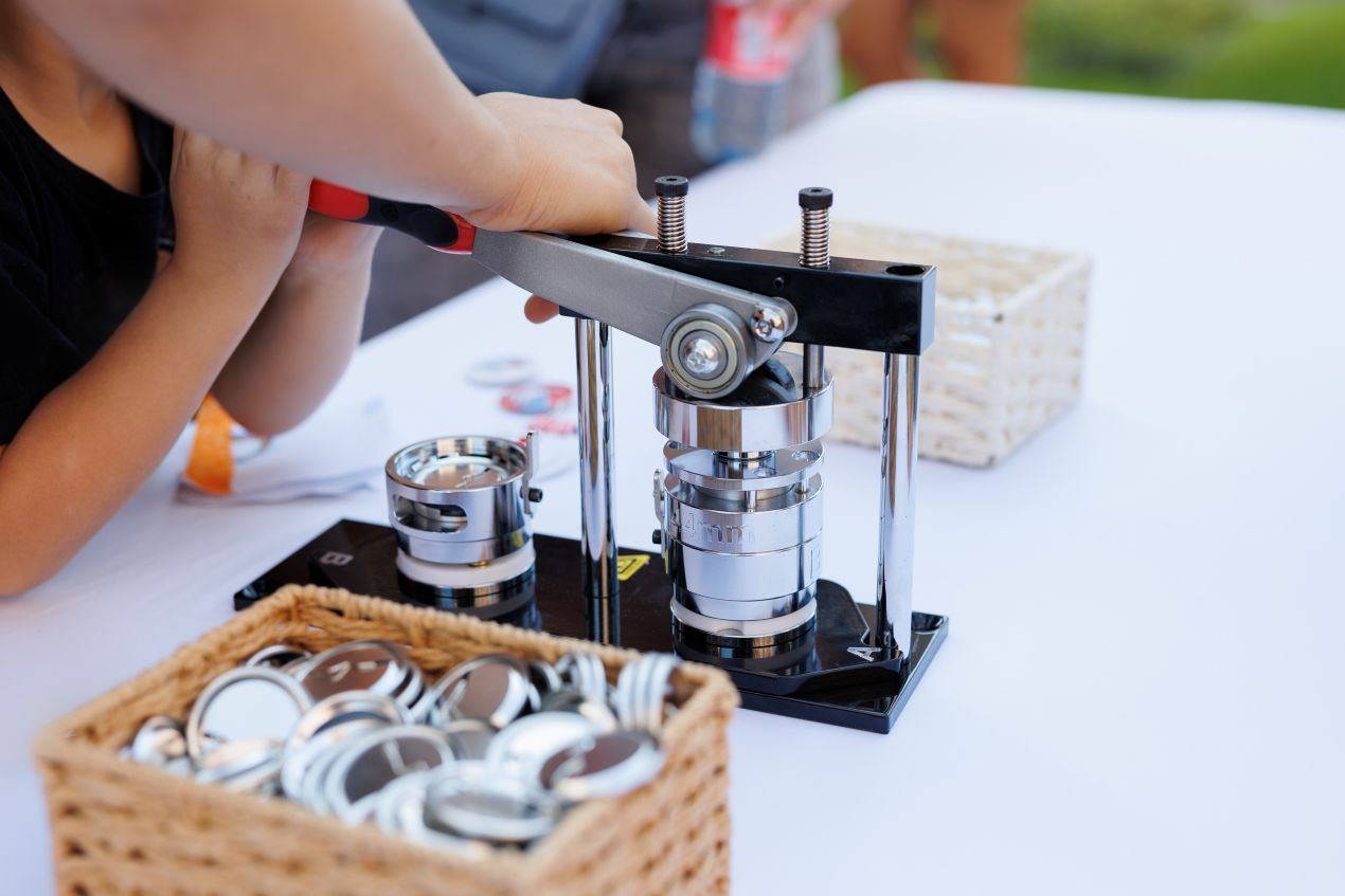 Ein Kind nutzt eine Buttonmaschine zum Herstellen eigener Anstecker – ideal fuer DIY-Projekte mit Familien und Schulkindern