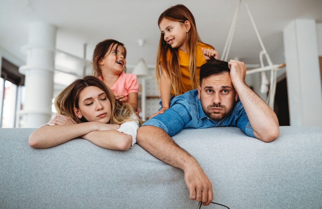 Eltern wirken erschoepft waehrend Kinder auf Sofa spielen | Alltagsbegleiter als Quereinsteiger