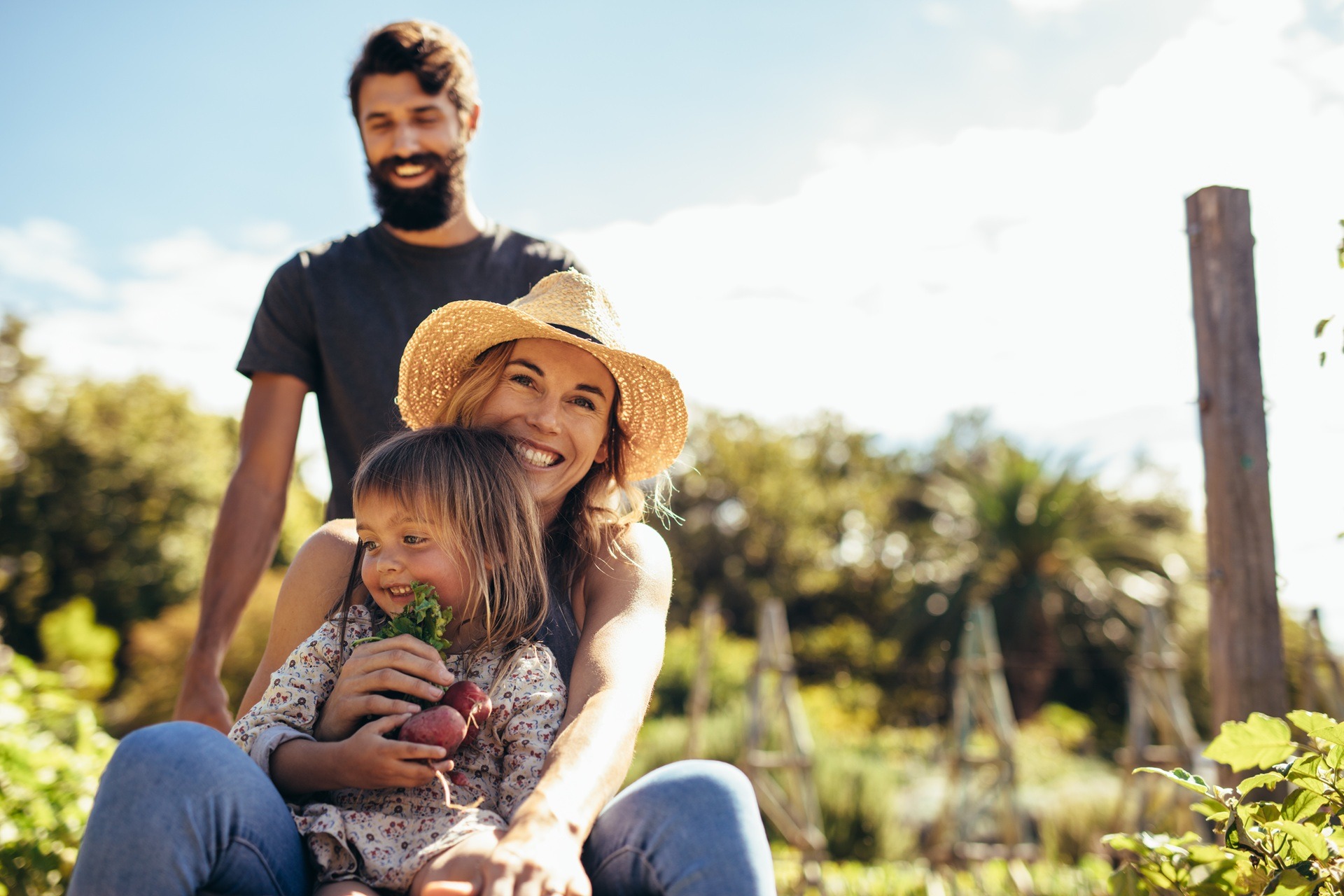 Familie sitzt lachend im Garten und hält frisches Gemüse | Cortenstahl Hochbeet